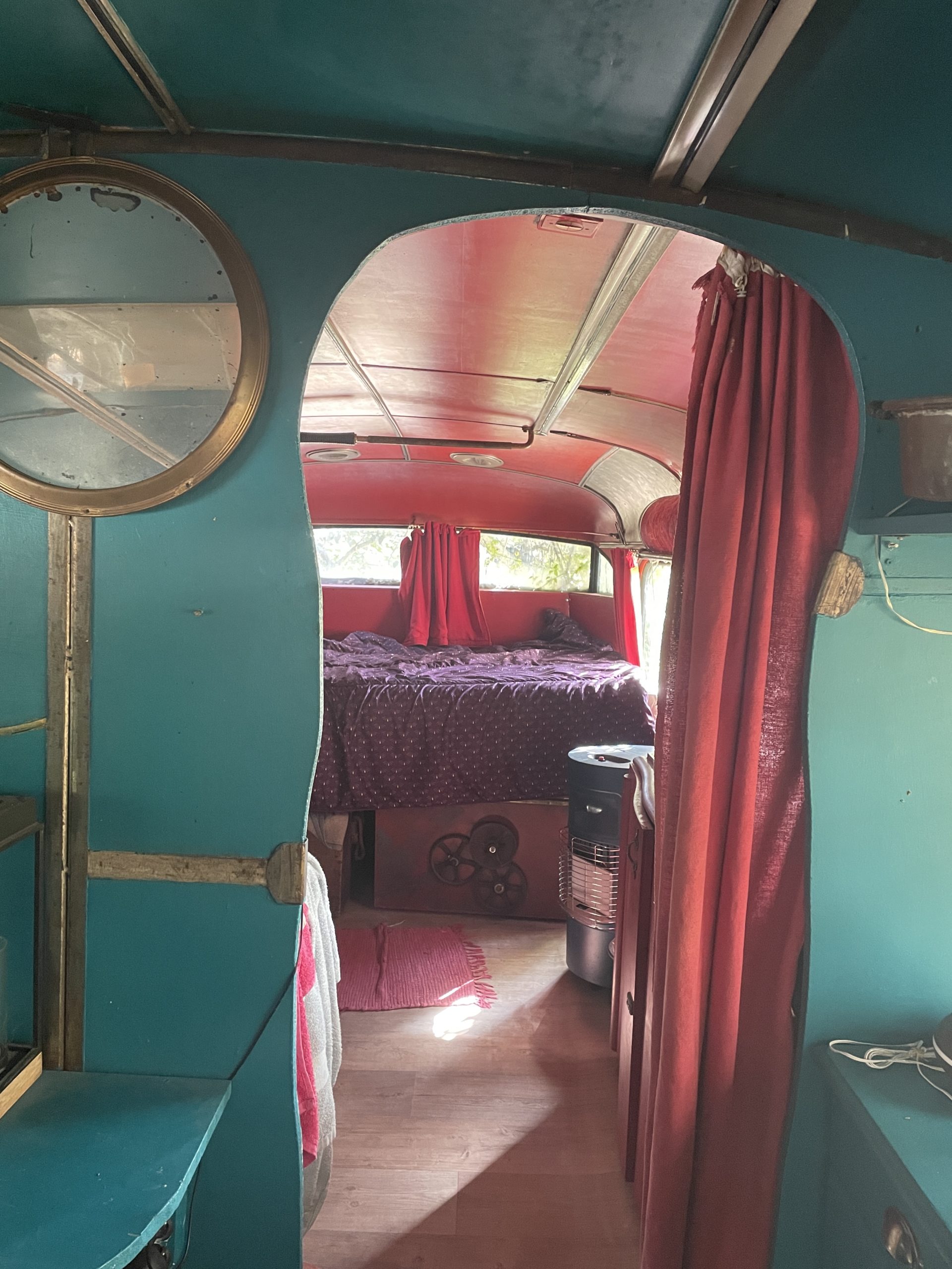 Photo de l'intérieur du car aménagé : la chambre, au fond du bus, peinte en rouge ; on aperçoit les fenêtre du bus